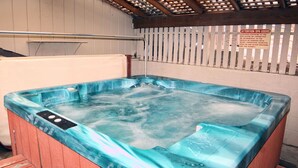 A hot tub with a wooden exterior and a blue interior, surrounded by a wooden deck and a white fence. - Timber Creek Chalets: 1 (Estes Park)
