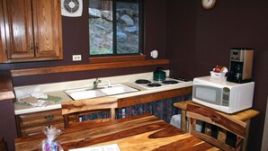 A compact kitchen with wooden cabinets, a sink, a microwave, and a window with a view of rocks. - Timber Creek Chalets: 1 (Estes Park)