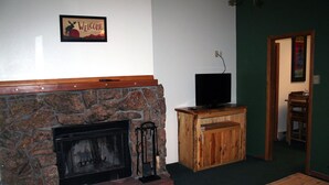 A stone fireplace with a television on top, a wooden cabinet, and a 'Welcome' sign on the wall. - Timber Creek Chalets: 1 (Estes Park)