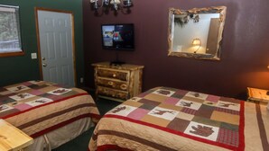 A room with two beds, a wooden dresser, a television, and a mirror on the wall. - Timber Creek Chalets: 1 (Estes Park)