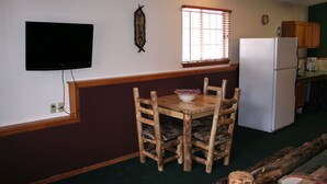 Une cuisine de taille réduite comprenant une table à manger en bois, des chaises, un téléviseur et un réfrigérateur.