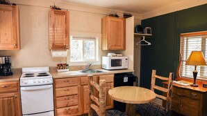 A compact kitchen with wooden cabinets, a stove, a microwave, and a dining area with two chairs.