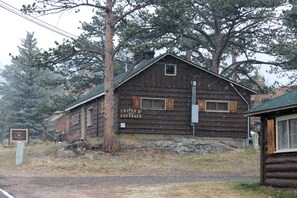 A rustic wooden cabin labeled "TRIPLE R COTTAGES" with a simple, functional design, surrounded by trees and a gravel path. - Triple R Cottages: 6 (Estes Park)