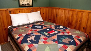 Une chambre à coucher avec une tête de lit en bois, une courtepointe à motifs animaliers et un panneau d’accueil représentant des ours.