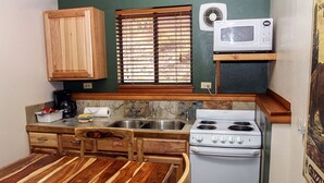 Une cuisine de taille réduite, dotée de meubles de rangement en bois, d’une cuisinière, d’un four à micro-ondes et d’une fenêtre avec des stores.