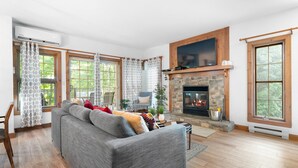 Una sala de estar con chimenea, ventanas amplias y un sofá gris.