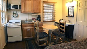 A compact kitchen with wooden cabinets, a microwave, a stove, a sink, and a round table with chairs. - Triple R Cottages: 7 (Estes Park)