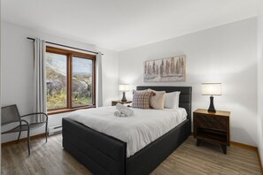 A bedroom with a bed, two bedside tables, a chair, a window with curtains, and a painting on the wall.