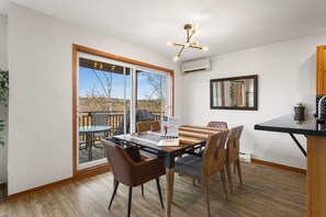 A dining area with a table and chairs, a ceiling light fixture, and a view through a glass door to the outdoors.