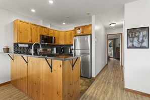 A modern kitchen with wooden cabinets, stainless steel appliances, and a black tiled backsplash.