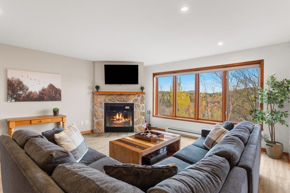 A modern living room with a stone fireplace, a large window with a view, and a flat-screen TV mounted above the fireplace.