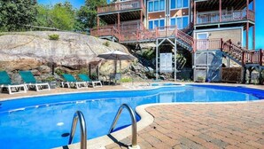 En swimmingpool med en terrass av tegelsten, solstolar och en byggnad med flera balkonger och trappor.