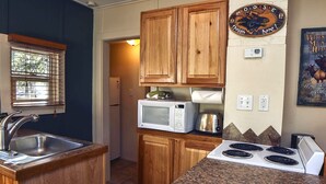 A compact kitchen with wooden cabinets, a granite countertop, a microwave, a toaster, and a stove. - Triple R Cottages: 2 (Estes Park)