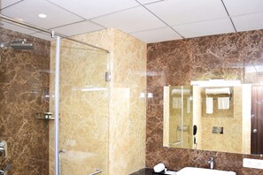 Um banheiro moderno com chuveiro envidraçado, um espelho grande e parede revestida em mármore.