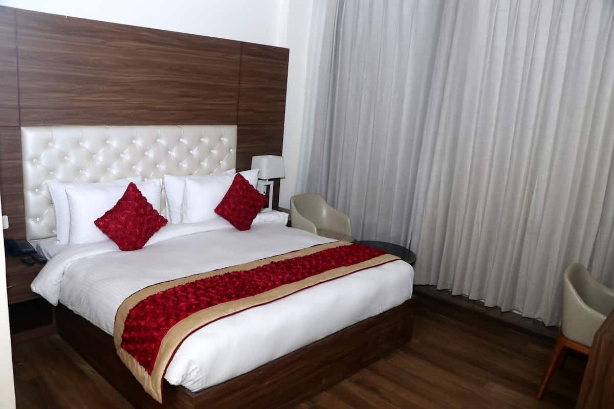 Habitación de hotel con una cama grande, cabecera de madera, mesita de noche con lámpara y una silla.