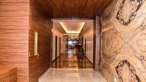 A modern hotel corridor with wooden paneling, marble walls, and a polished floor.