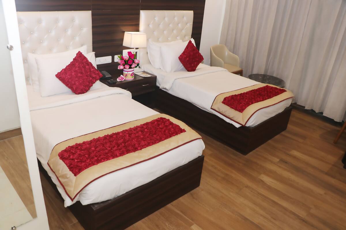 Habitación de hotel con dos camas, cada una con colcha y almohadas a juego color rojo. Entre las camas, una mesita de noche con una lámpara y un florero con flores.