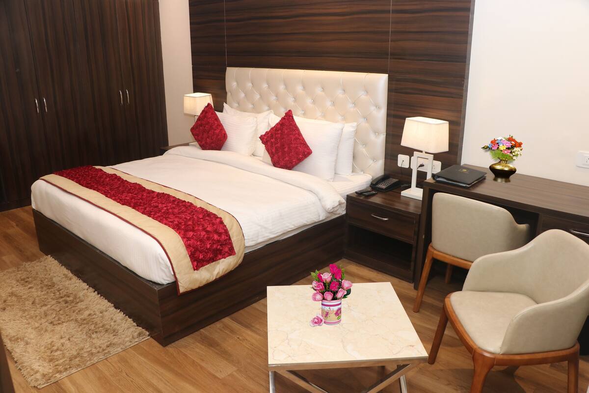 Habitación de hotel con una cama grande, un escritorio con lámpara, una silla y una mesita con un jarrón de flores.