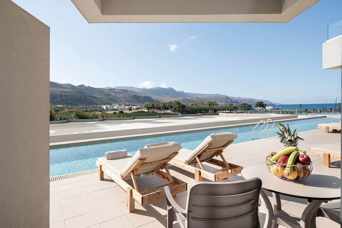 A poolside area with lounge chairs, a table with fruit, and a view of a mountain and sea.