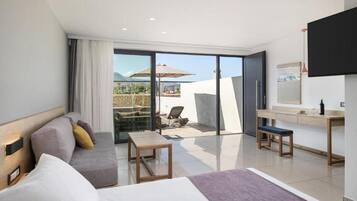 Habitación de hotel moderna con un amplio ventanal corredero que da a un patio, un sofá, una mesita, un banco y un televisor montado en la pared.