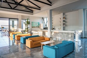 Un vestíbulo de hotel moderno con zonas de estar, una recepción y un amplio ventanal con vistas al exterior.