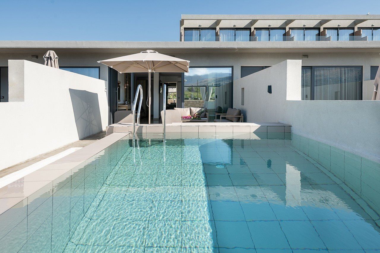 Un área de piscina moderna con agua cristalina, una tumbona y una zona de estar cubierta.