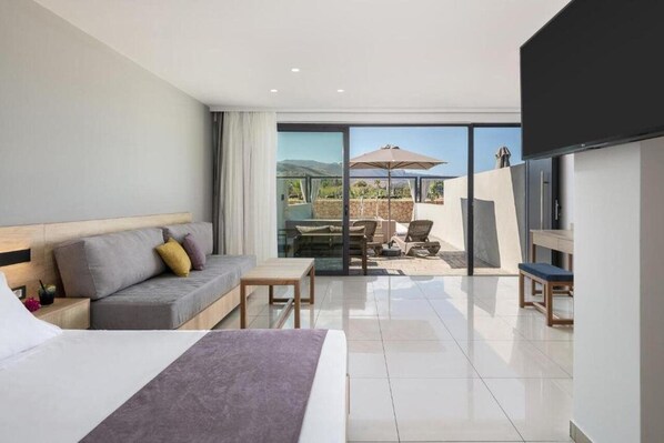 Una habitación de hotel moderna con una cama grande, un sofá, una mesita y un balcón con mobiliario exterior.