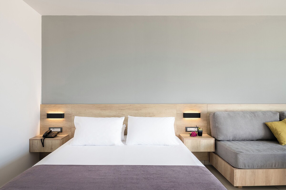 Una habitación de hotel moderna con cama, mesitas de noche, sofá y cabecero de madera.