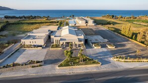 A large, modern building with a flat roof, surrounded by a parking area and landscaped gardens. - Chq Galini Palace (Platanias)