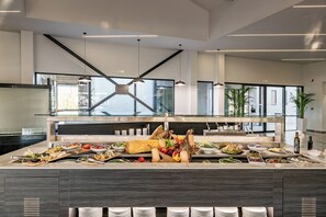 A modern buffet setup with various food items and a glass partition. - Chq Galini Palace (Platanias)