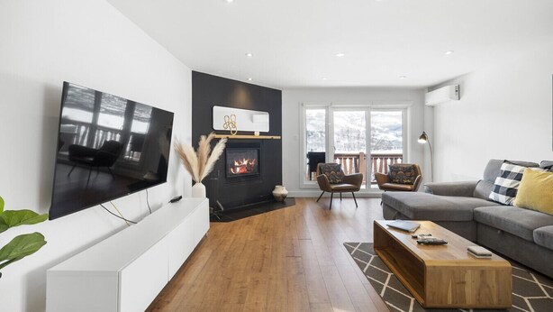 Ein modernes Wohnzimmer mit Flachbildfernseher, Kamin, zwei Sesseln, einer Couch und einem Couchtisch.
