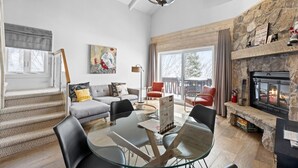 A spacious living room with a fireplace, a staircase, and a large window.