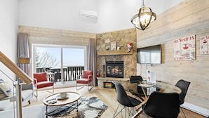 A spacious living room with a fireplace, a dining area, and a balcony with outdoor seating.