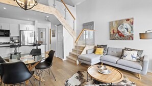 A modern living space with a staircase, a gray sofa, a dining area, and a kitchen.