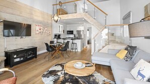 A modern living room with a TV, dining area, and a staircase leading to a kitchen and upper level.
