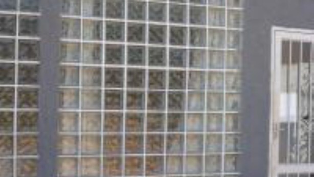 Un edificio con grandes ventanales con barrotes de metal, una puerta visible y una pared exterior gris.
