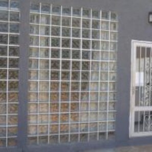 A building with large windows featuring metal bars, a visible door, and a grey exterior wall. - Monoambiente el Yguazu (Puerto Iguazú)