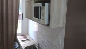 Una cocina pequeña con microondas, pileta y ventana con cortinas.