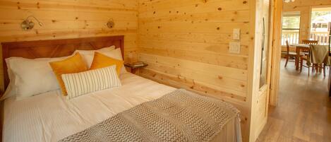 Une chambre dans une cabane en bois, avec un lit, des oreillers, une table de chevet et une vue sur la salle à manger.