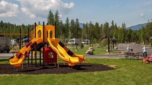 A playground with slides and a picnic area, surrounded by trees and a parking lot. - West Glacier Cabin Village (West Glacier)