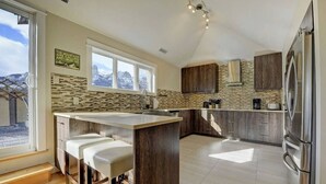 Cozinha moderna com uma ilha grande, banquetas, forno embutido e vista para montanhas pelas janelas.
