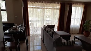 Een woonkamer met een bank, een eettafel met stoelen en een groot raam met gordijnen.