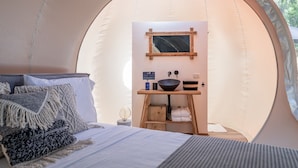 Una tenda acollidora amb un llit, una taula de fusta petita amb un rentapeus, i un mirall.