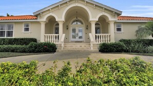 A two-story house with a symmetrical facade, a central entrance with a white door, and a balcony on the second floor. - Elegance Redefined, Simply Seconds Away from the Beach! (Marco Island)