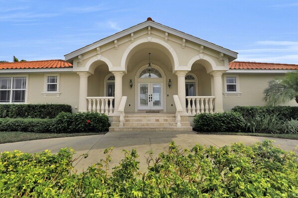 A two-story house with a symmetrical facade, a central entrance with a white door, and a balcony on the second floor.