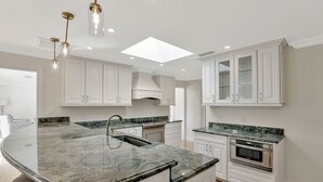 A modern kitchen with white cabinetry, a large island with a granite countertop, stainless steel appliances, and pendant lighting. - Elegance Redefined, Simply Seconds Away from the Beach! (Marco Island)