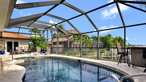 A swimming pool with a glass enclosure, surrounded by lounge chairs and a patio area. - Elegance Redefined, Simply Seconds Away from the Beach! (Marco Island)