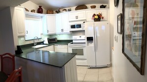 A kitchen with white cabinets, a black countertop, a stove, an oven, a microwave, and a refrigerator. - CP 421 2 Bedroom Ocean View Condo - Paradise Vacation Rental in Ocean Village (Fort Pierce)