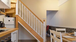 Une cuisine avec un escalier en bois, des meubles blancs et un coin repas avec des chaises et une table, le tout dans des tons blancs.