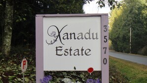 Letrero de Nanadu Estate con el número '370', rodeado de follaje y flores.